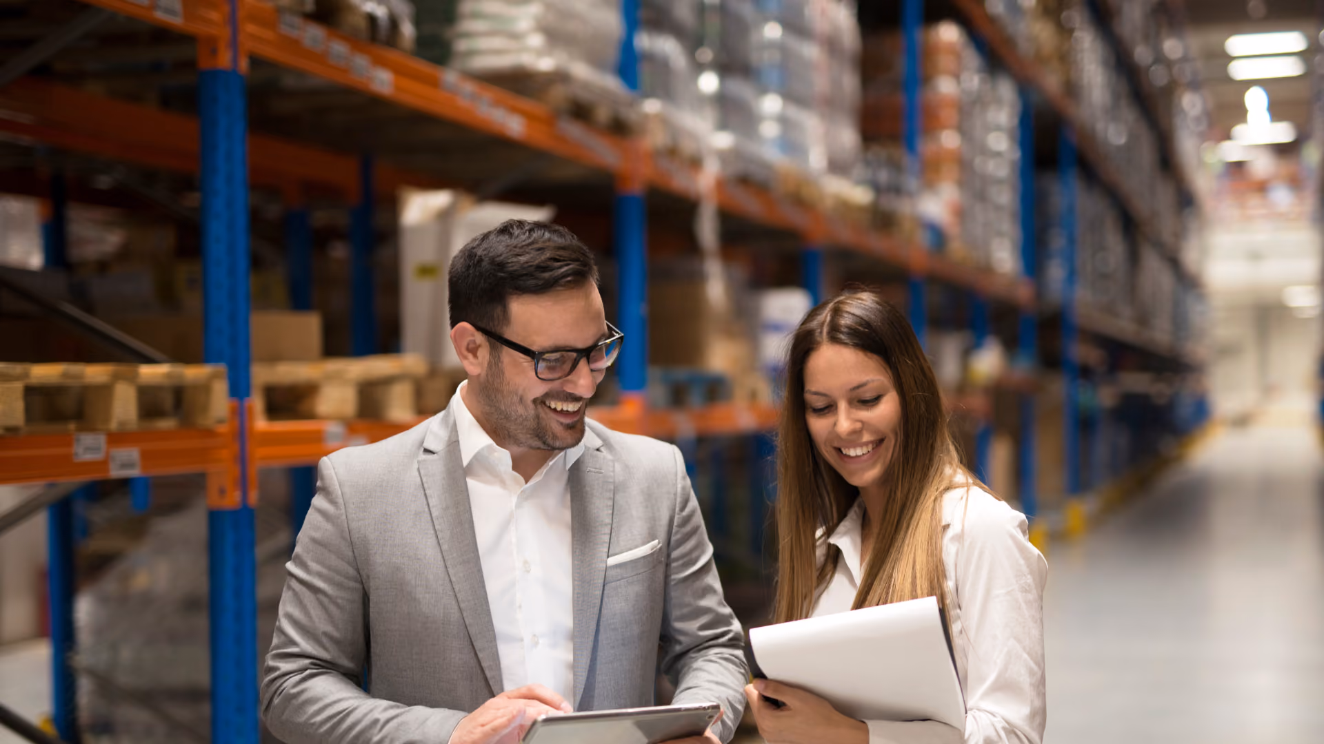 Two logistics manager smiling, looking at a laptop inside a warehouse