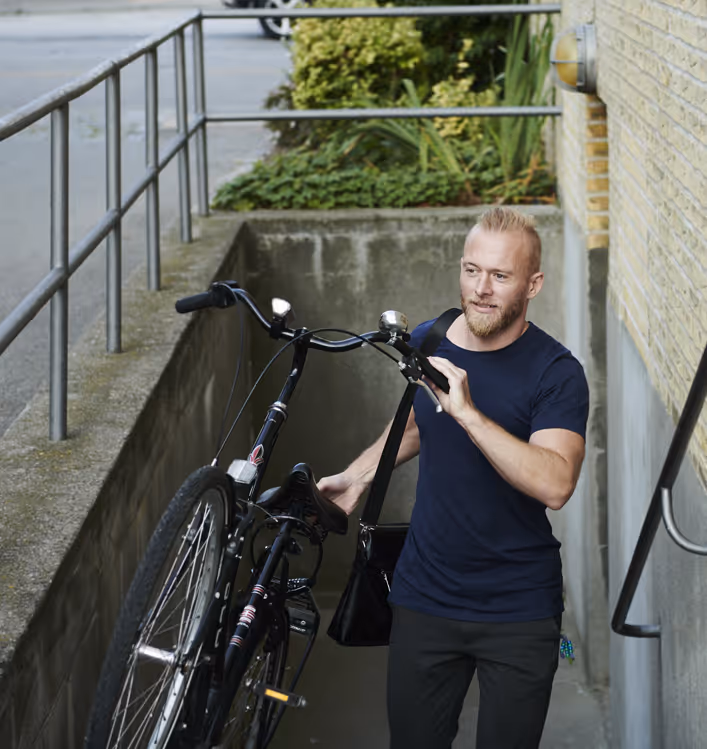 En ung mann bærer en sykkel opp fra en kjellerbod til gatenivå.