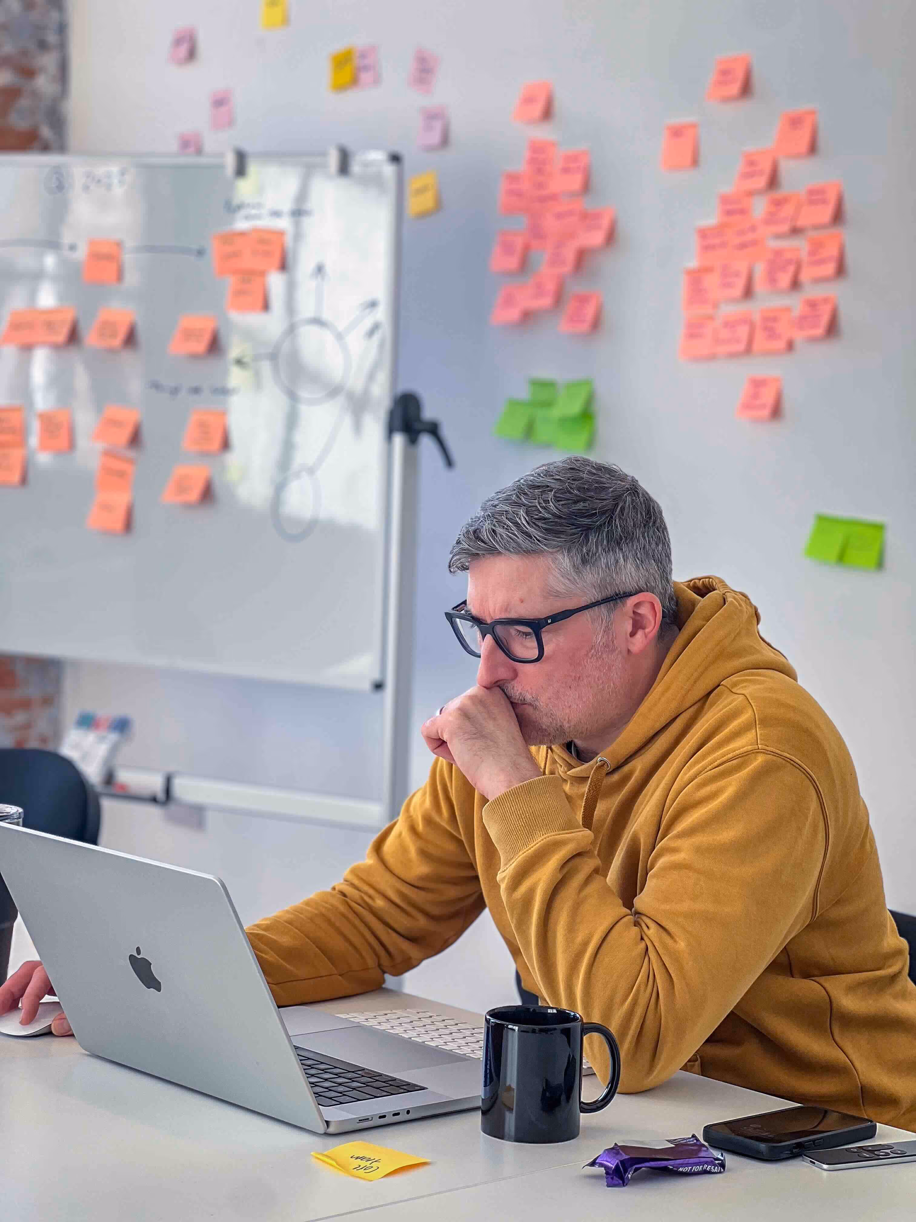 A man wearing glasses and a yellow sweater is working on a laptop.