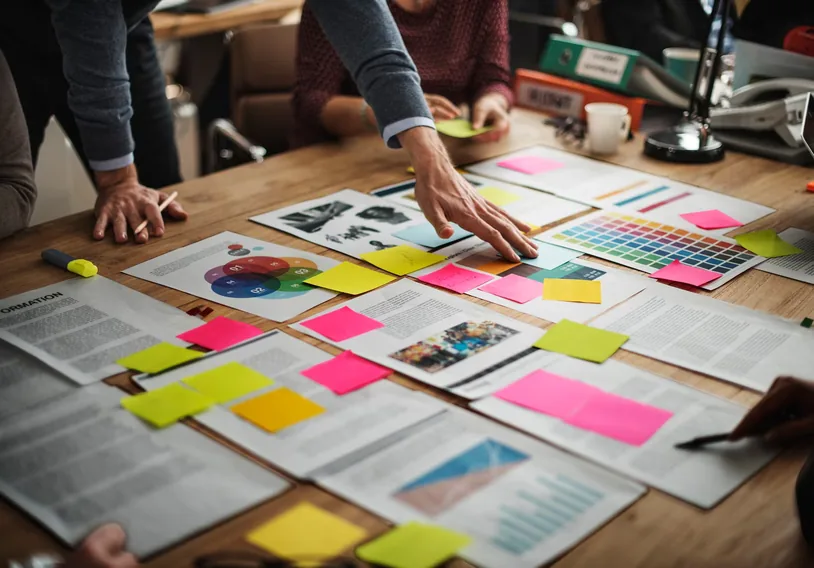 Team reviewing colourful sticky notes and printed charts spread across a table