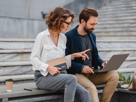Two colleagues reviewing work on a laptop outdoors