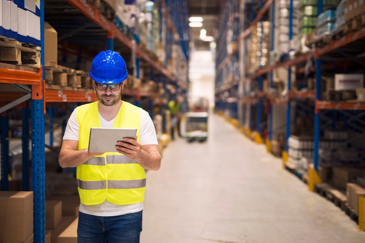 Warehouse worker in a hard hat checking a tablet