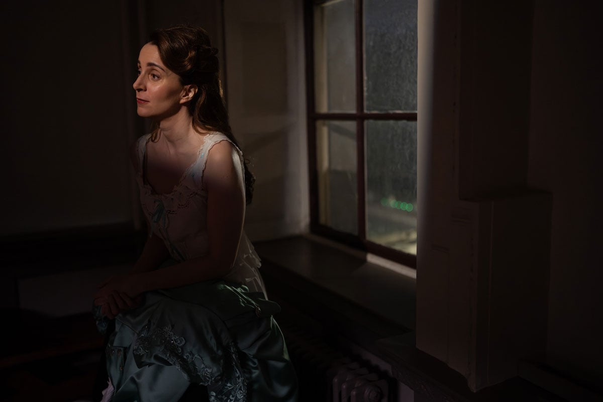 An Edwardian era woman sits in a window, tense