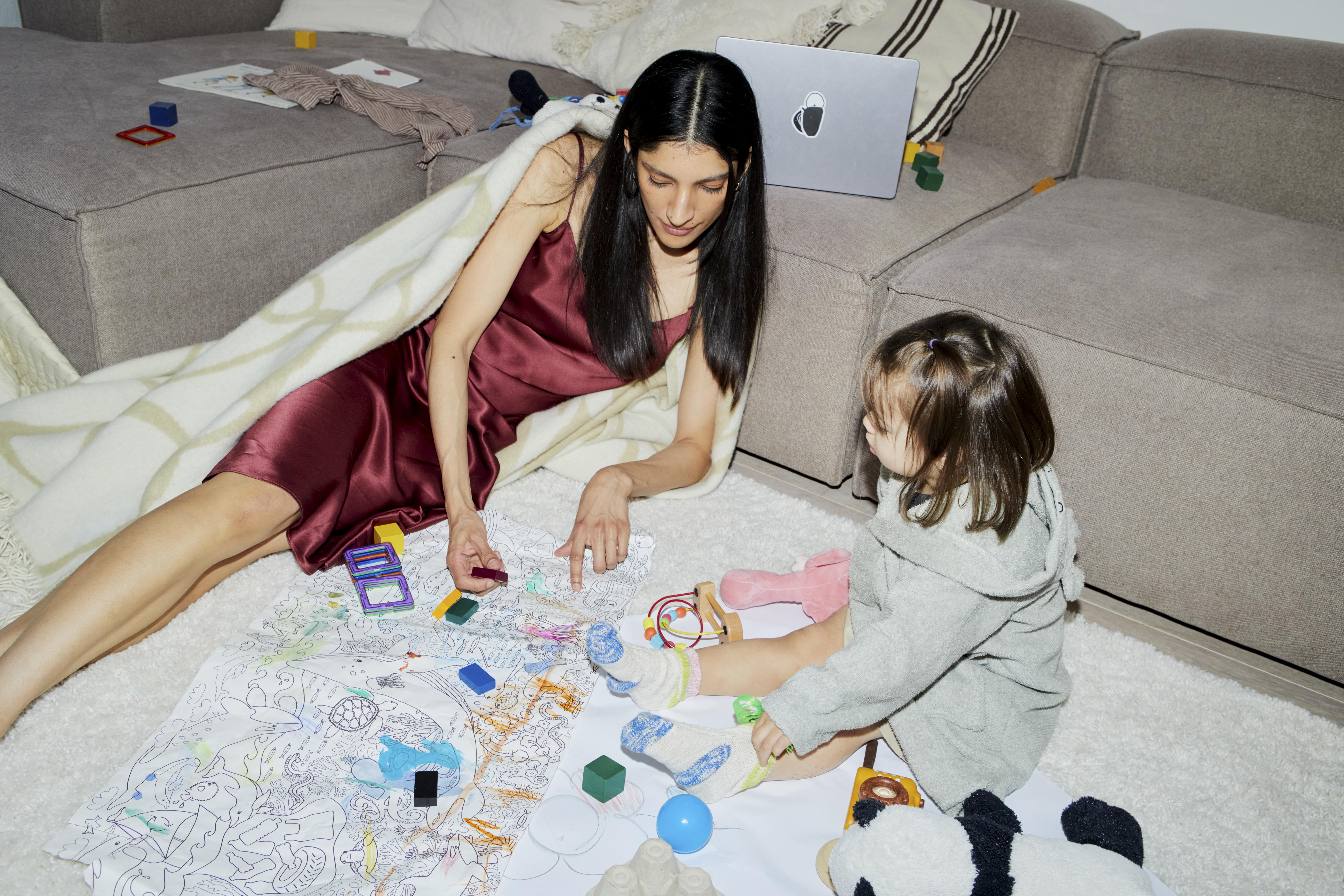 A woman playing with a kid laying on the floor