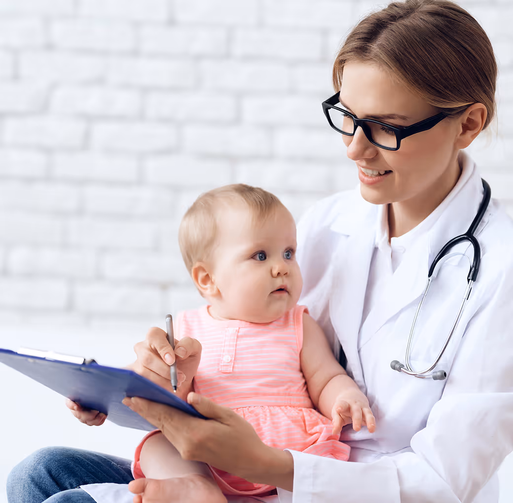Pediatrician holding a baby while writing on medical forms.