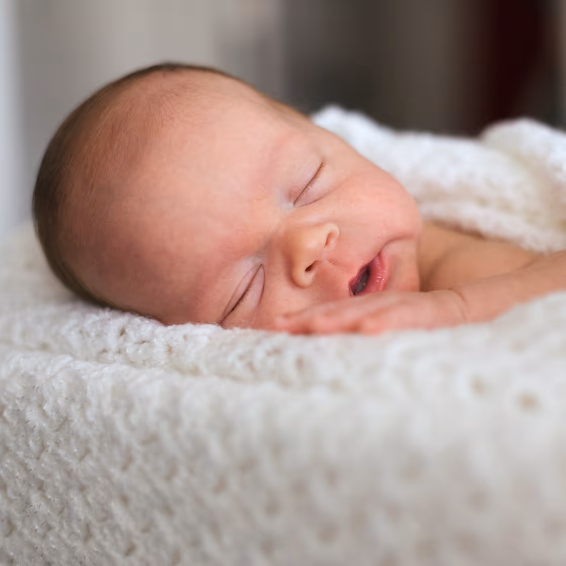 Newborn baby peacefully sleeping while swaddled in a blanket.