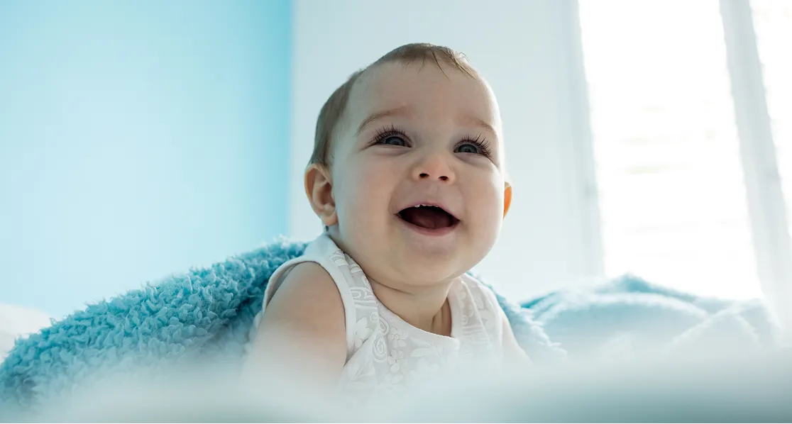Smiling baby wrapped in a blue blanket with a light blue background.