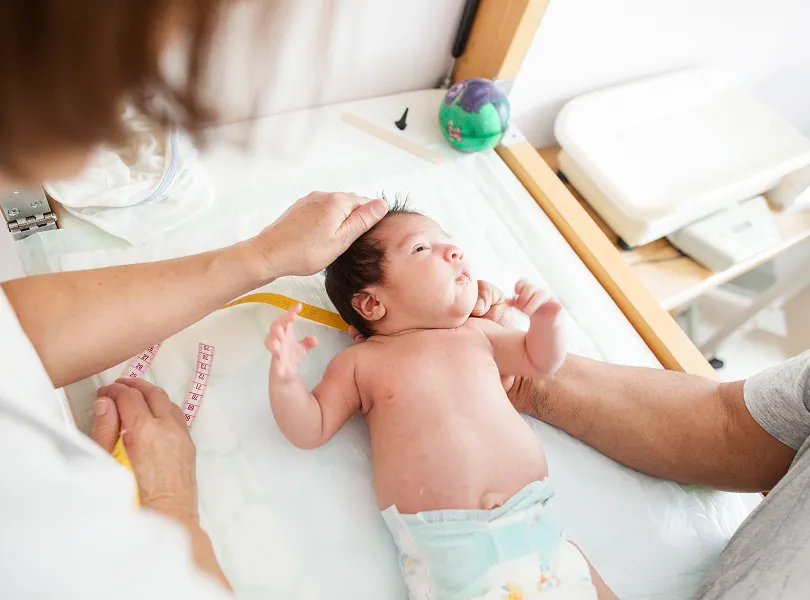 Healthcare professional measuring newborn baby's head with a tape during a medical checkup.