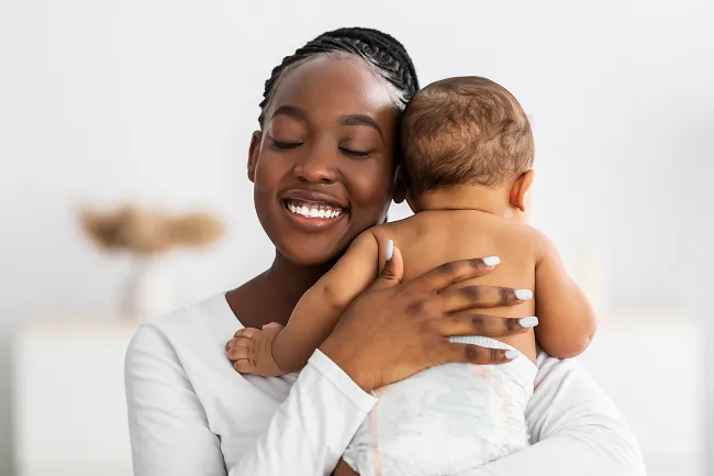 Smiling mother holding and hugging her baby wearing a diaper.