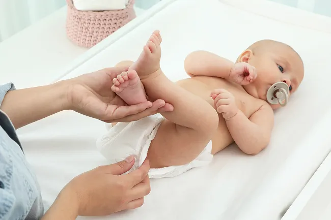 Adult hands gently cleaning a newborn baby lying on a changing table with a pacifier in mouth.