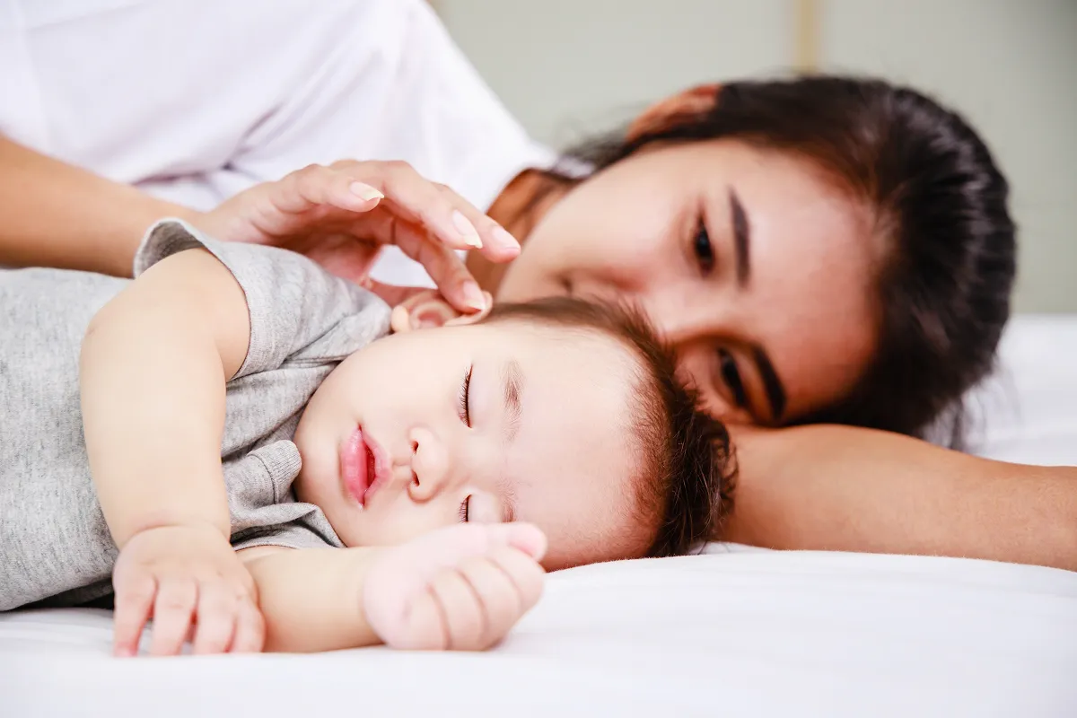 La madre toca y cuida suavemente a su bebé dormido acostado en una cama.