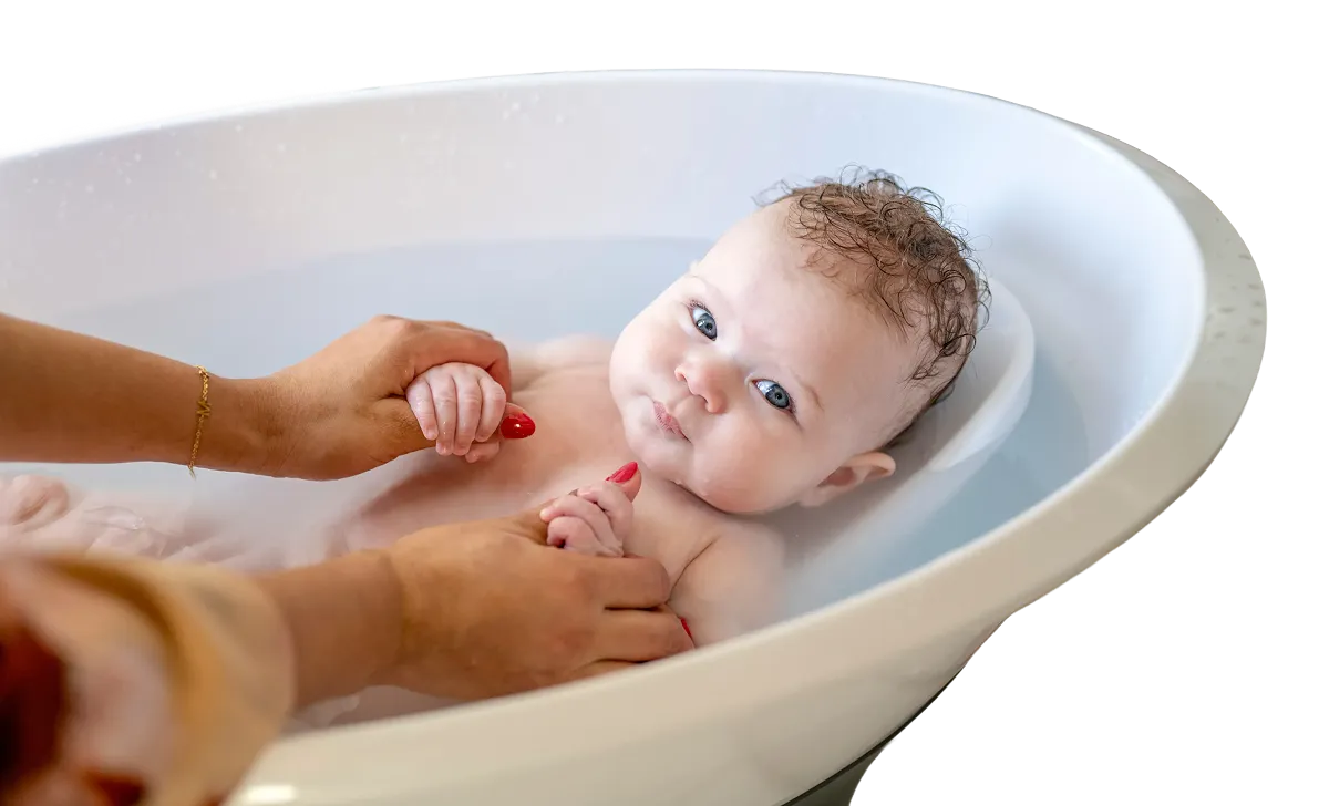 Smiling baby sitting in a white plastic baby bathtub.