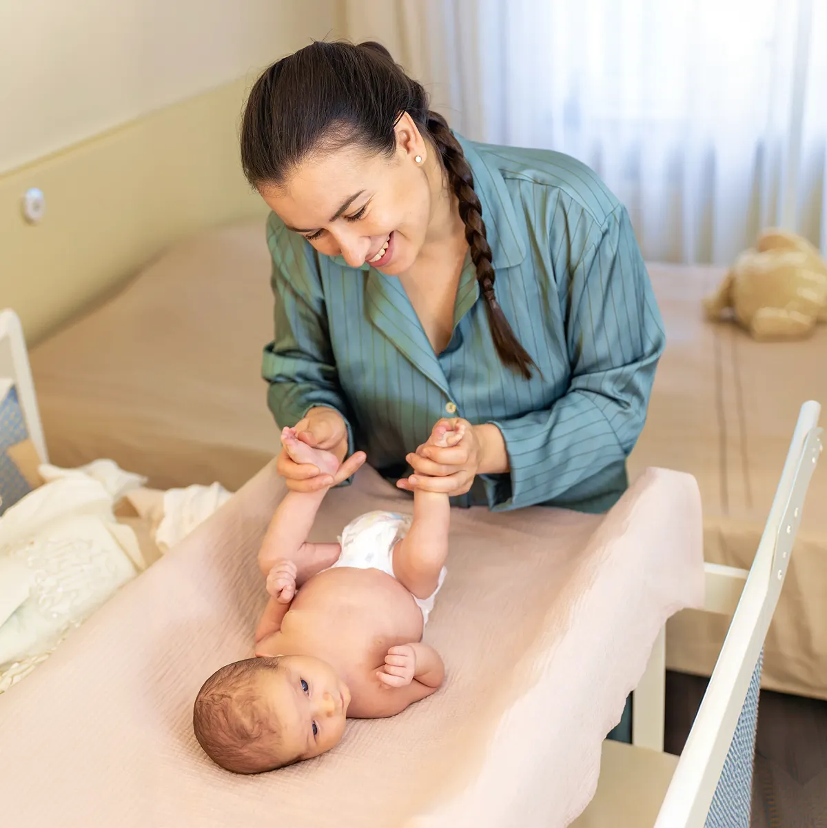 Smiling mother holding her baby’s hands while changing the baby’s diaper on a changing table.