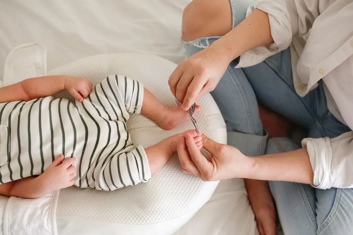 Madre acostada en la cama sosteniendo al bebé por encima de ella, sonriendo y tocándose la nariz.