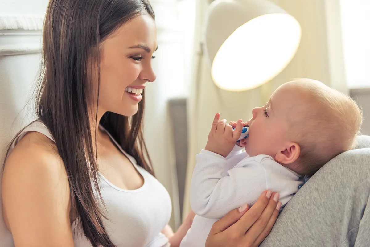 Ti bebe k ap dòmi, li gen yon onesie ble trikote sou li, kouche nan yon bèso an bwa ak dra ki gen modèl zetwal.
