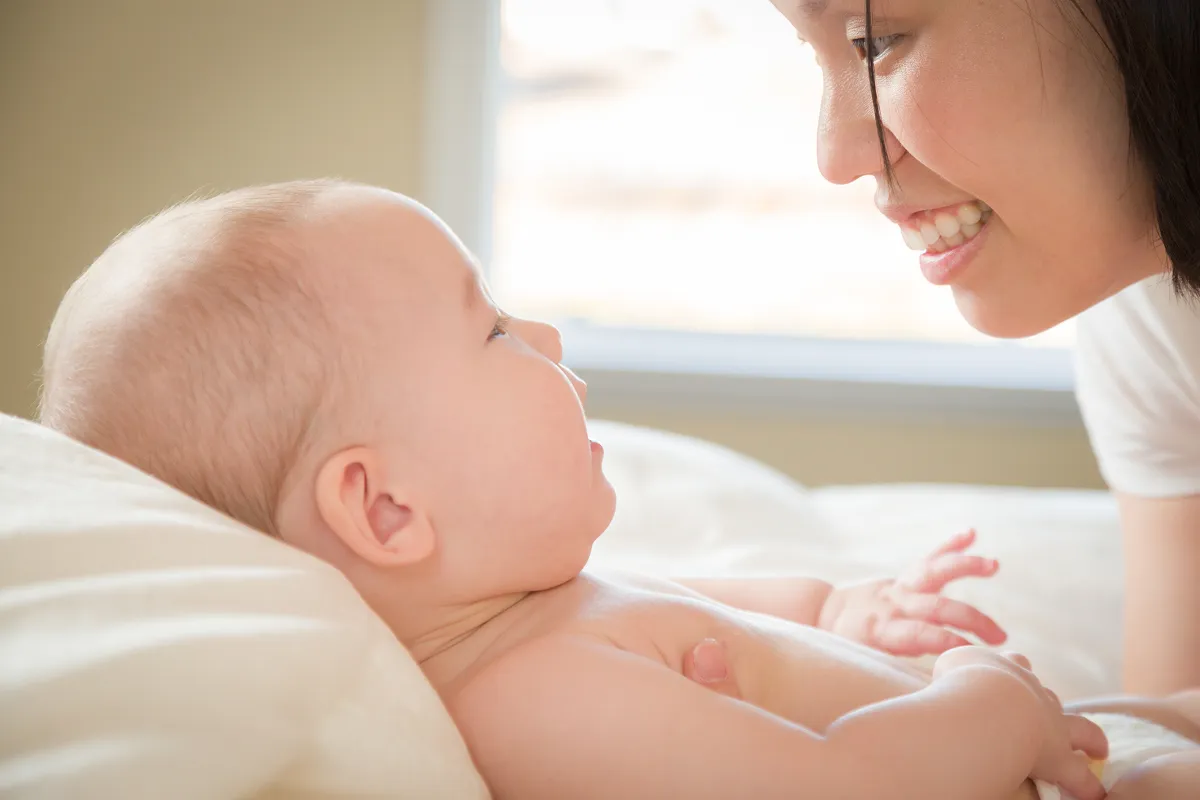Yawning baby lying on a textured white blanket with arms raised.