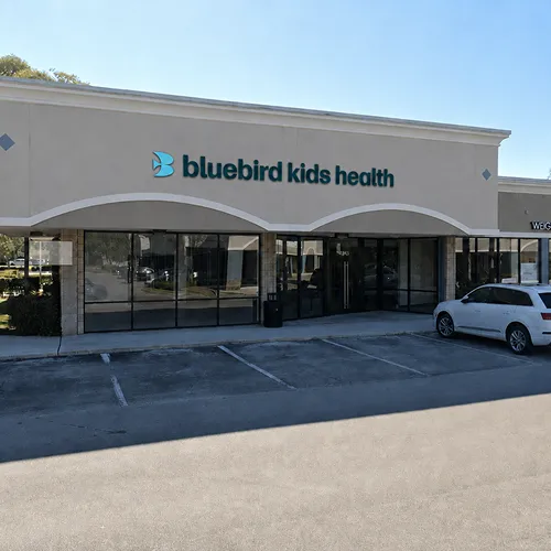 Exterior of Bluebird Kids Health clinic with a white car parked outside on a sunny day.