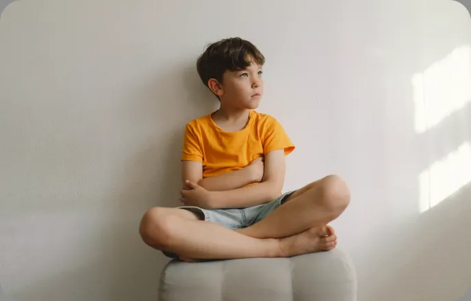 An image of a boy sitting in front of a laptop, covering his face.