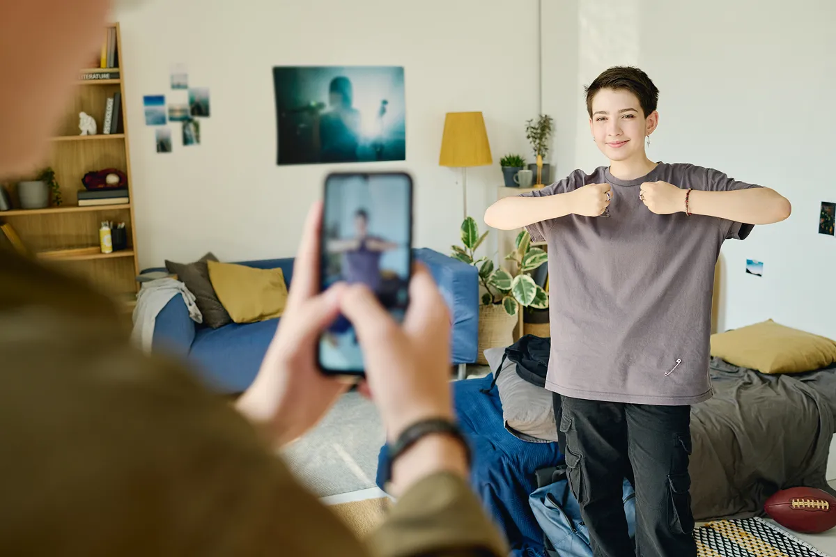 Happy teenage girl showing dance exercise while looking at camera of smartphone