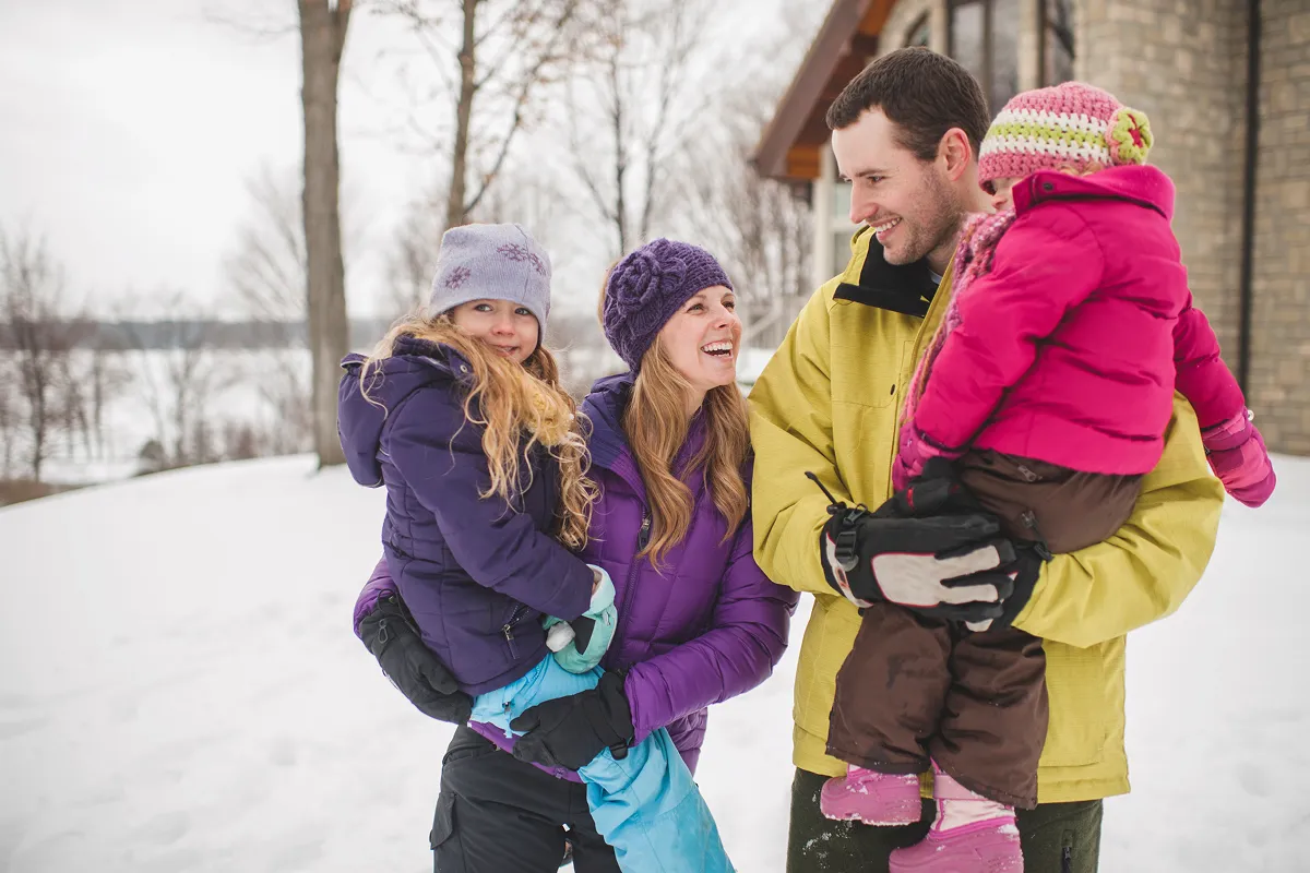 Mother and father carrying daughters in snow