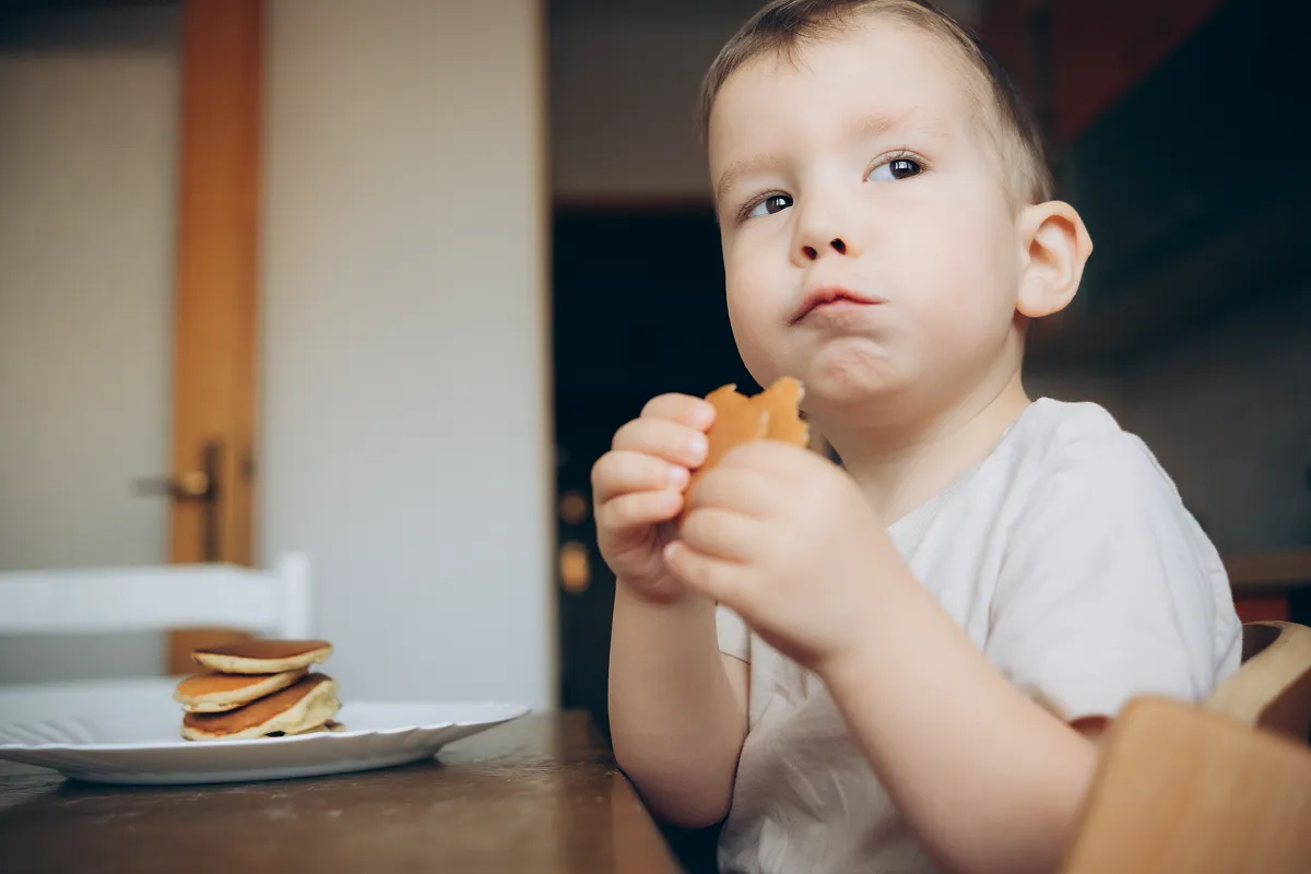 Happy little boy eating pancakes. Portrait of small cute little boy child sitting by the table at ho