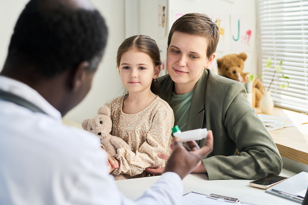 Pediatrician explaining an inhaler to a mother and her young daughter in a pediatric exam room