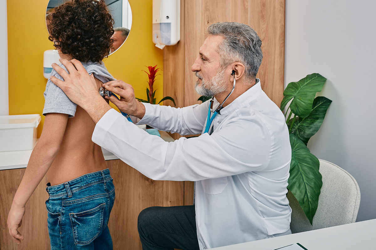 Pediatrician using a stethoscope to listen to a boy's back during a school physical