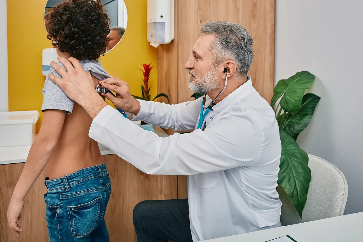 Pediatrician using a stethoscope to listen to a boy's back during a school physical