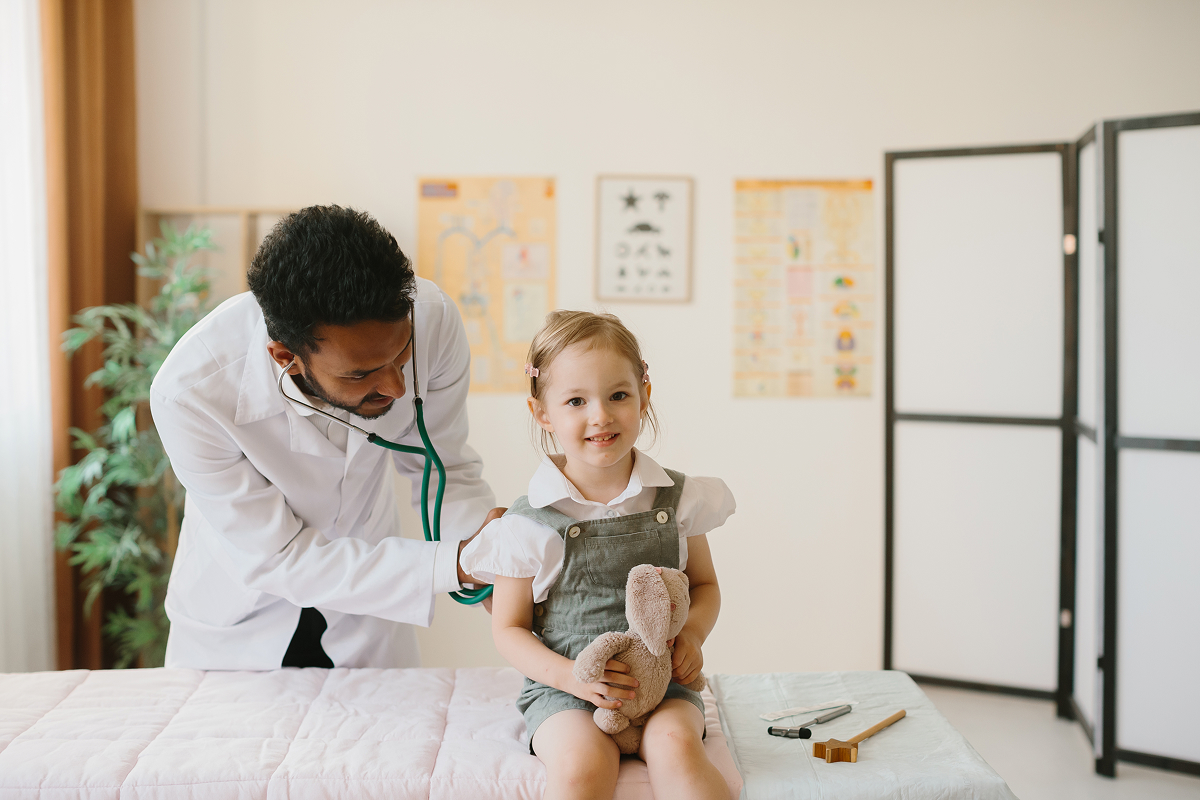 Pediatrician listening to a smiling young girl's chest with a stethoscope at a checkup