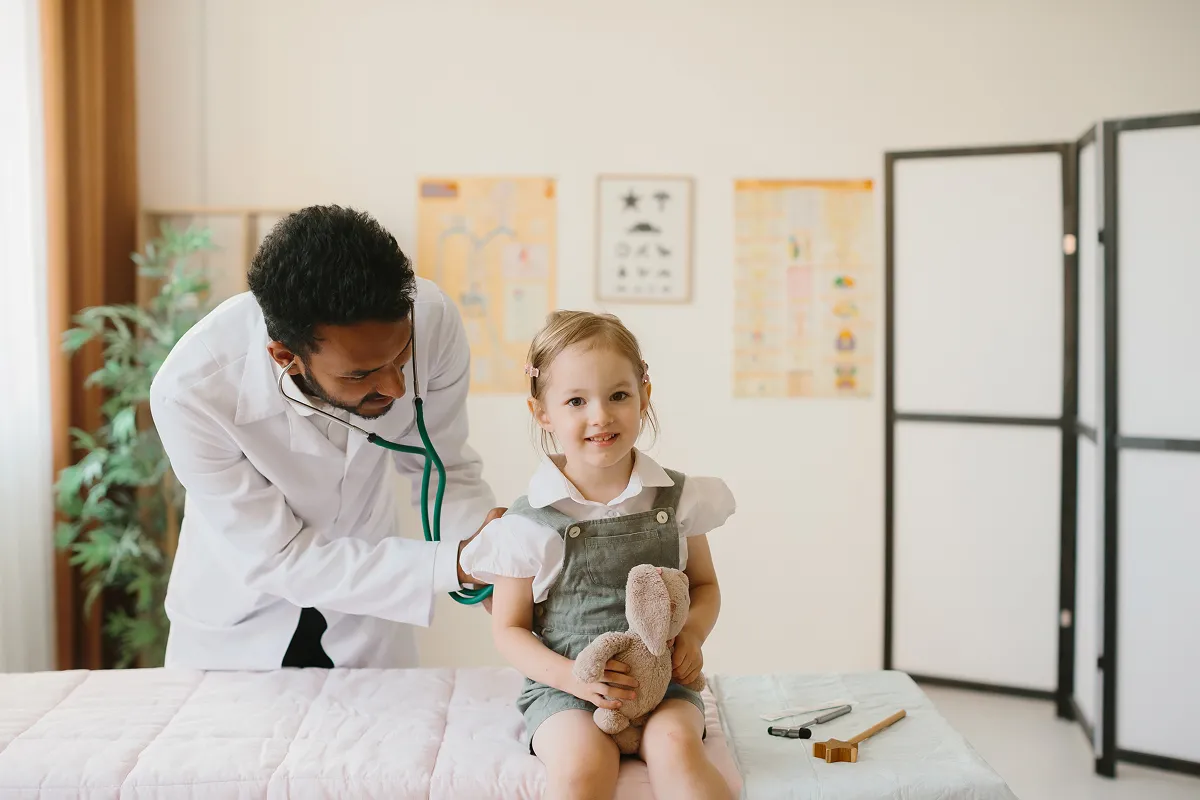 Pediatrician listening to a smiling young girl's chest with a stethoscope at a checkup
