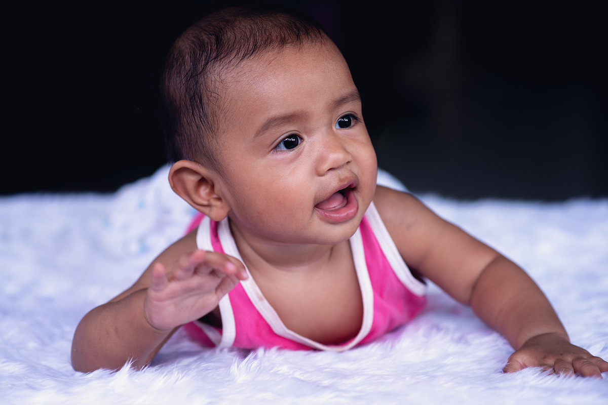Baby in a pink top propped up on their arms during tummy time on a fluffy white blanket