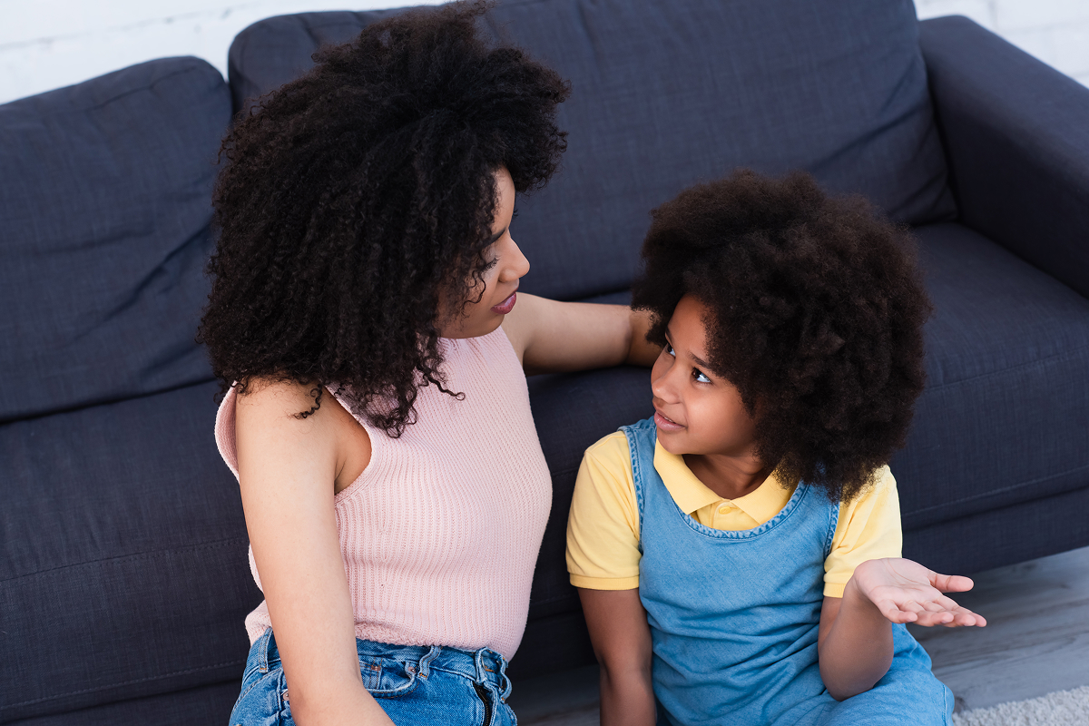 Mother and daughter sitting beside a sofa having a conversation at home