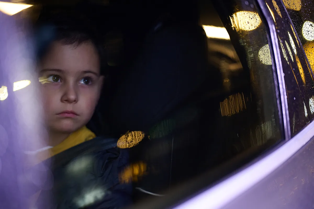 Young boy sitting in the back seat of a car at night with rain running down the windows