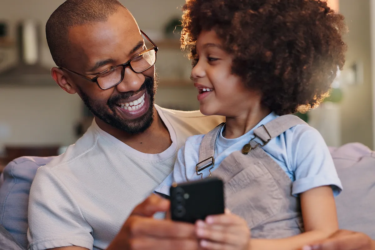 Father and young child laughing together while watching something on a phone at home