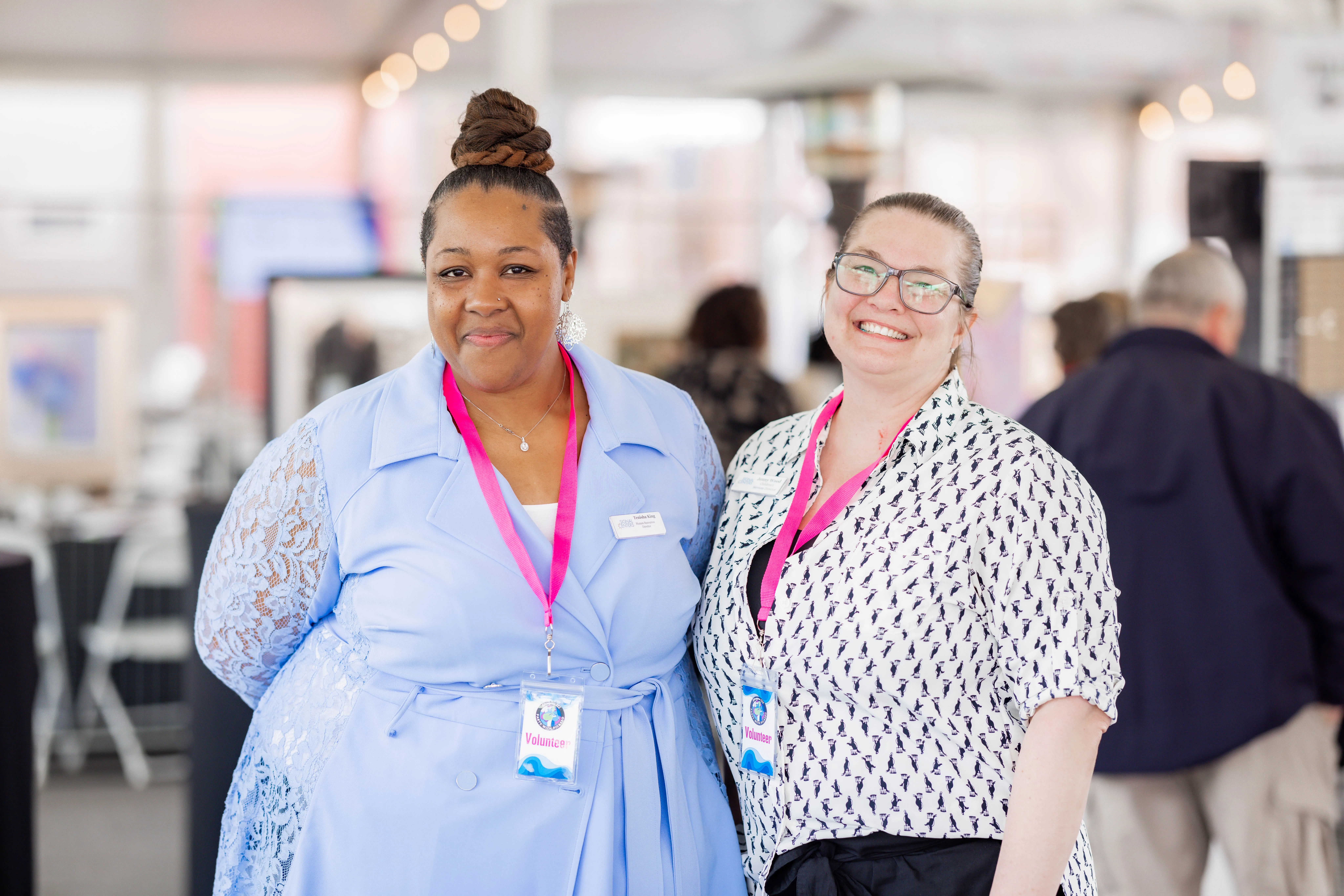 Two women smiling with pink lanyards on