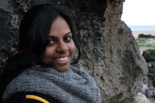 Photo of me, Anusha, a brown woman of Indian origin, stood against a rocky cave smiling at the camera.