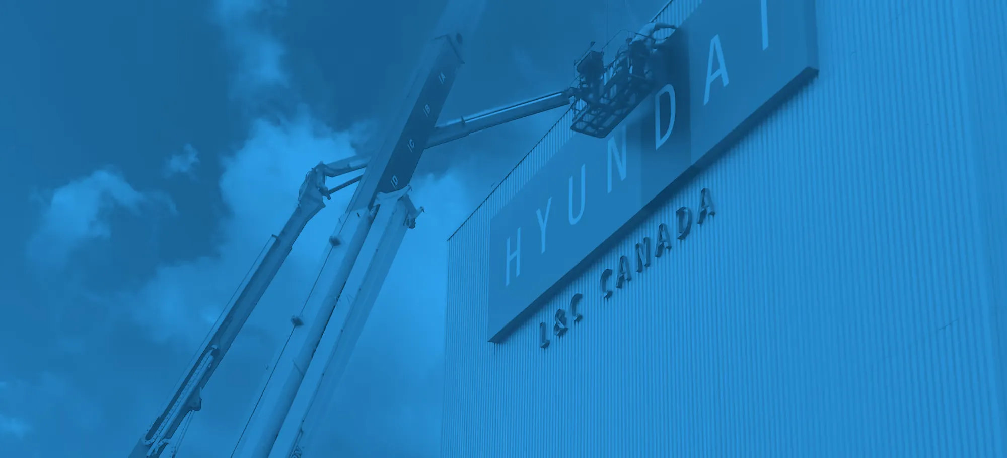 An Excellent Sign Group crew installing a large illuminated Hyundai sign on a building facade from a boom lift.