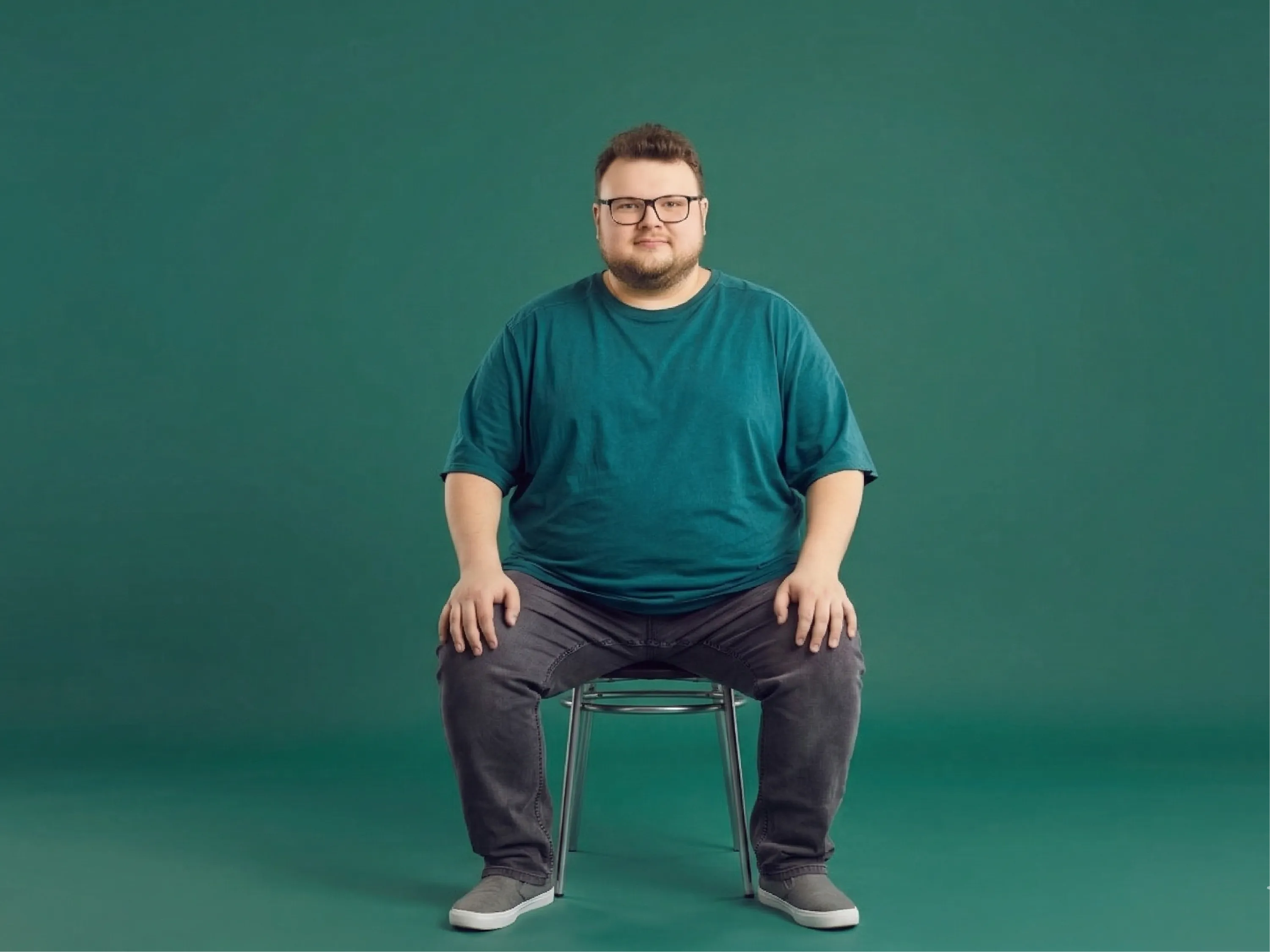 Ein Mann sitzt auf dem Sofa und isst Gebäck, was typische Adipositas und Übergewicht Ursachen wie Bewegungsmangel und ungesunde Ernährung veranschaulicht.