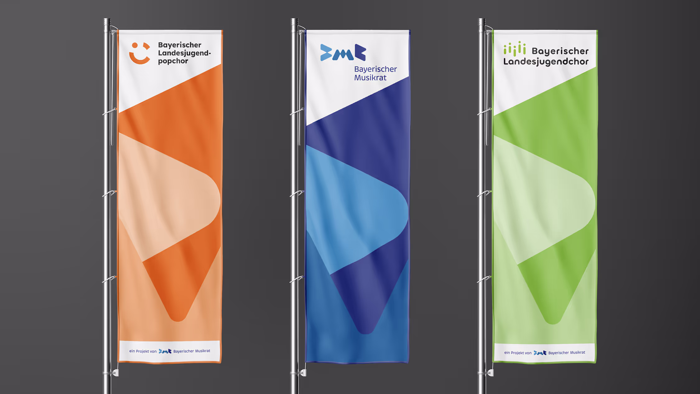 Drei vertikale Flaggen sind auf Metallstangen vor dunklem Hintergrund angebracht, die jeweils für verschiedene Abteilungen des „Bayerischen Musikrats“ stehen. Die linke Flagge ist orange und mit der Aufschrift „Bayerischer Landesjugendpopchor“ versehen. In der oberen linken Ecke befindet sich ein stilisiertes Smiley-Logo. Die mittlere Flagge ist blau und trägt oben das weiße Logo des „Bayerischen Musikrats“. Die rechte Flagge ist grün und steht für den „Bayerischen Landesjugendchor“. Das Logo besteht aus senkrechten Balken, die an Schallwellen erinnern. Jede Flagge hat ein modernes geometrisches Design mit überlappenden Formen in verschiedenen Farbnuancen und eine weiße Fußzeile, in der darauf hingewiesen wird, dass es sich um Projekte des „Bayerischen Musikrats“ handelt.