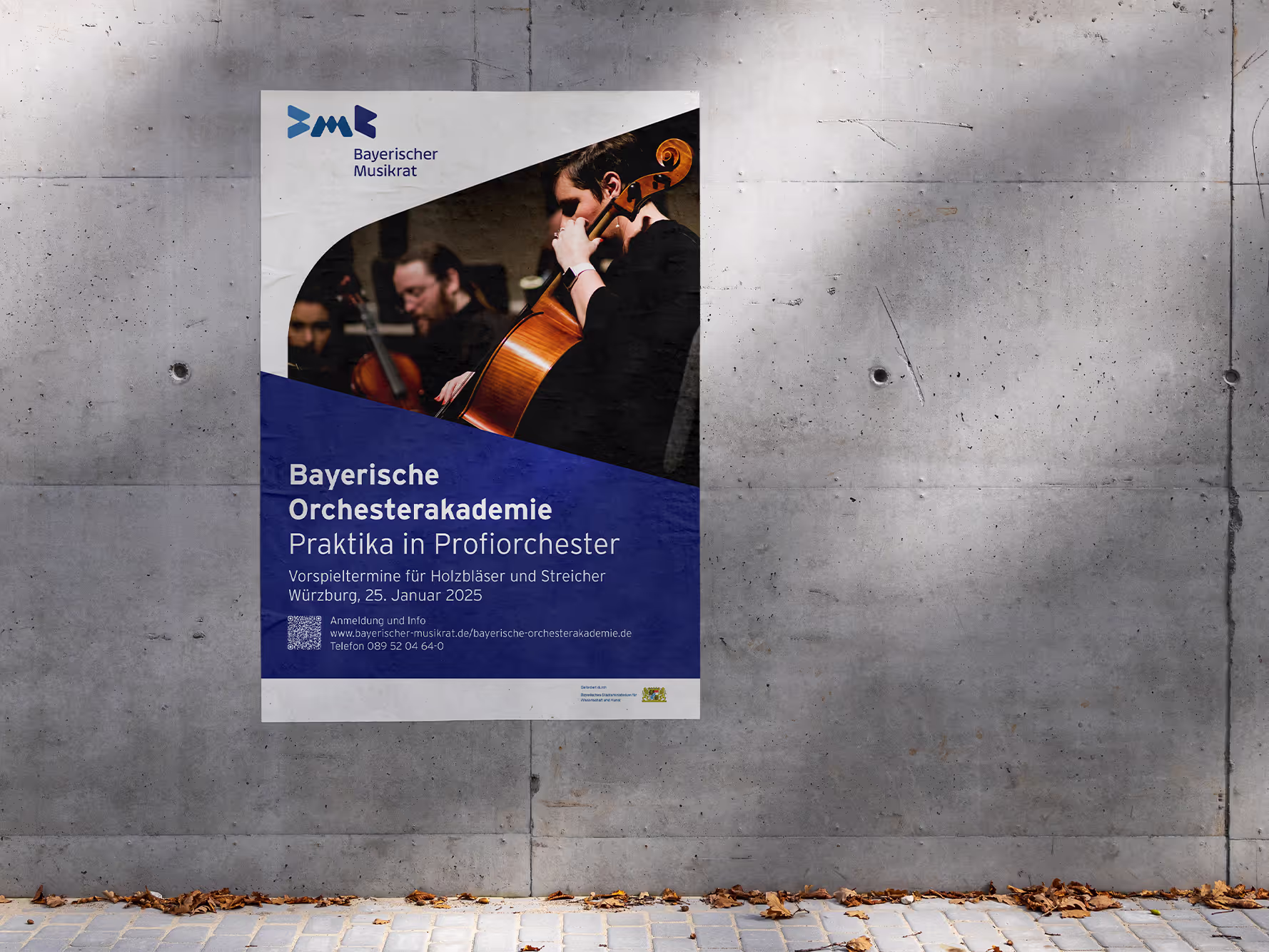 An einer modernen Betonwand im Außenbereich ist ein Plakat angebracht, das für die „Bayerische Orchesterakademie“ wirbt. Das Poster zeigt ein Foto eines jungen Musikers, der Cello spielt, während andere Orchestermusiker im Hintergrund leicht verschwommen sind. Der obere Teil enthält das Logo des „Bayerischen Musikrats“, und der untere Teil hat ein blaues geometrisches Design mit weißem Text, der die Veranstaltungsdetails enthält. Der Text erwähnt eine Gelegenheit für Holzbläser und Streicher, am 25. Januar 2025 in Würzburg vorzuspielen, zusammen mit einem Link zur Website und Kontaktinformationen. Der Boden unter dem Poster ist mit abgefallenen Blättern gesäumt, und die Kulisse erinnert an einen öffentlichen Raum oder einen Universitätscampus.