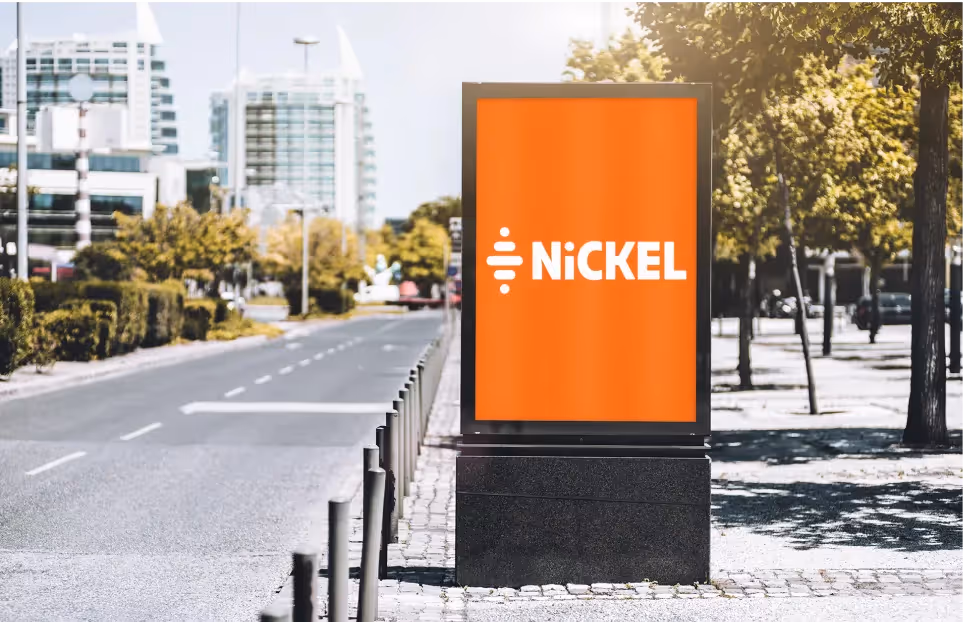 An outdoor advertising display on a city sidewalk showing a bright orange ad with the word ‘Nickel’ in white text