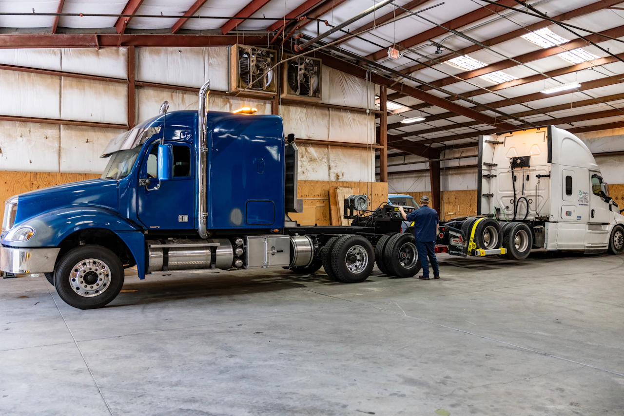 Two semi trucks, one blue, one white in a repair bay.