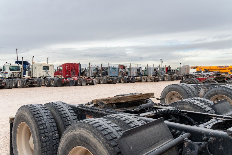 Heavy-duty truck chassis lined up in a repair yard, with Sterling crane equipment in the background.