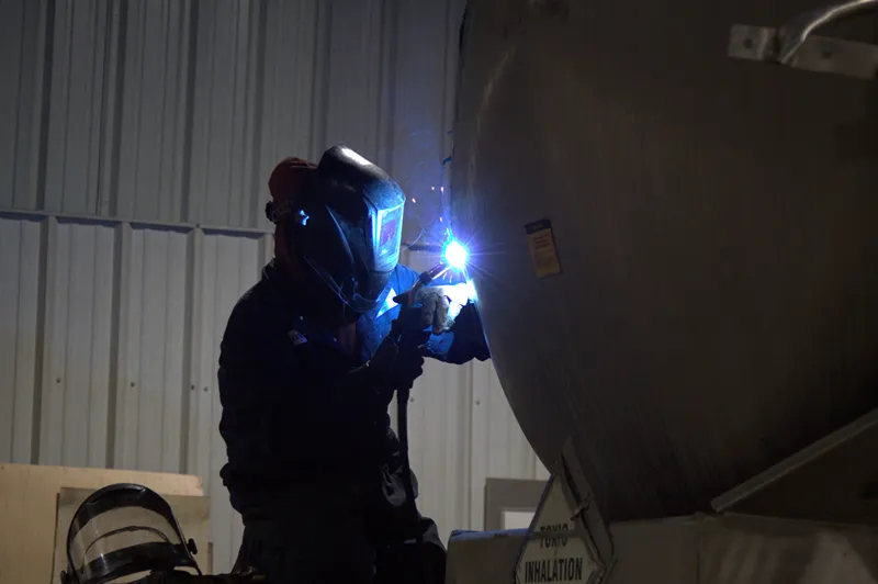 R stamp welding on an industrial pressure vessel, with a welder at work. Visible text reads "INHALATION."