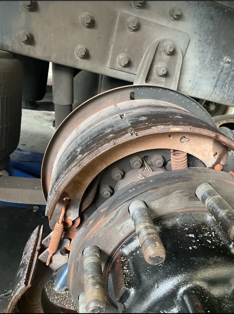 Heavy-duty truck brake repair showing a worn brake drum, shoes, springs, and exposed wheel hub components.