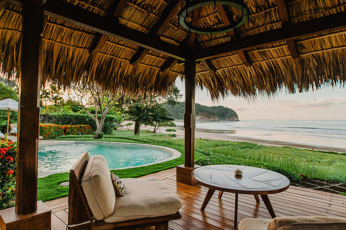 An outdoor dining or relaxation area set on the sand under palm trees near the beach