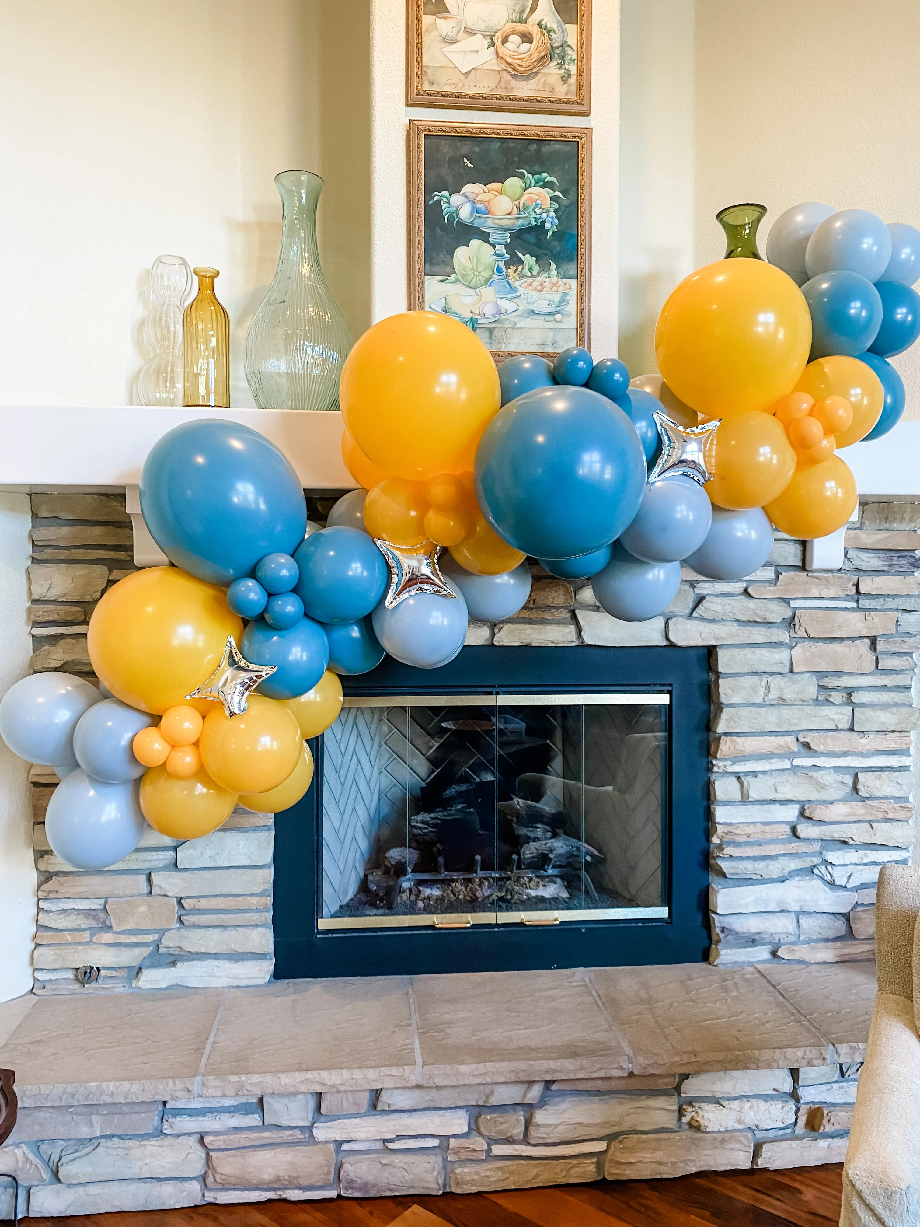 Blue and yellow balloon garland with silver star accents arranged across a stone fireplace mantel