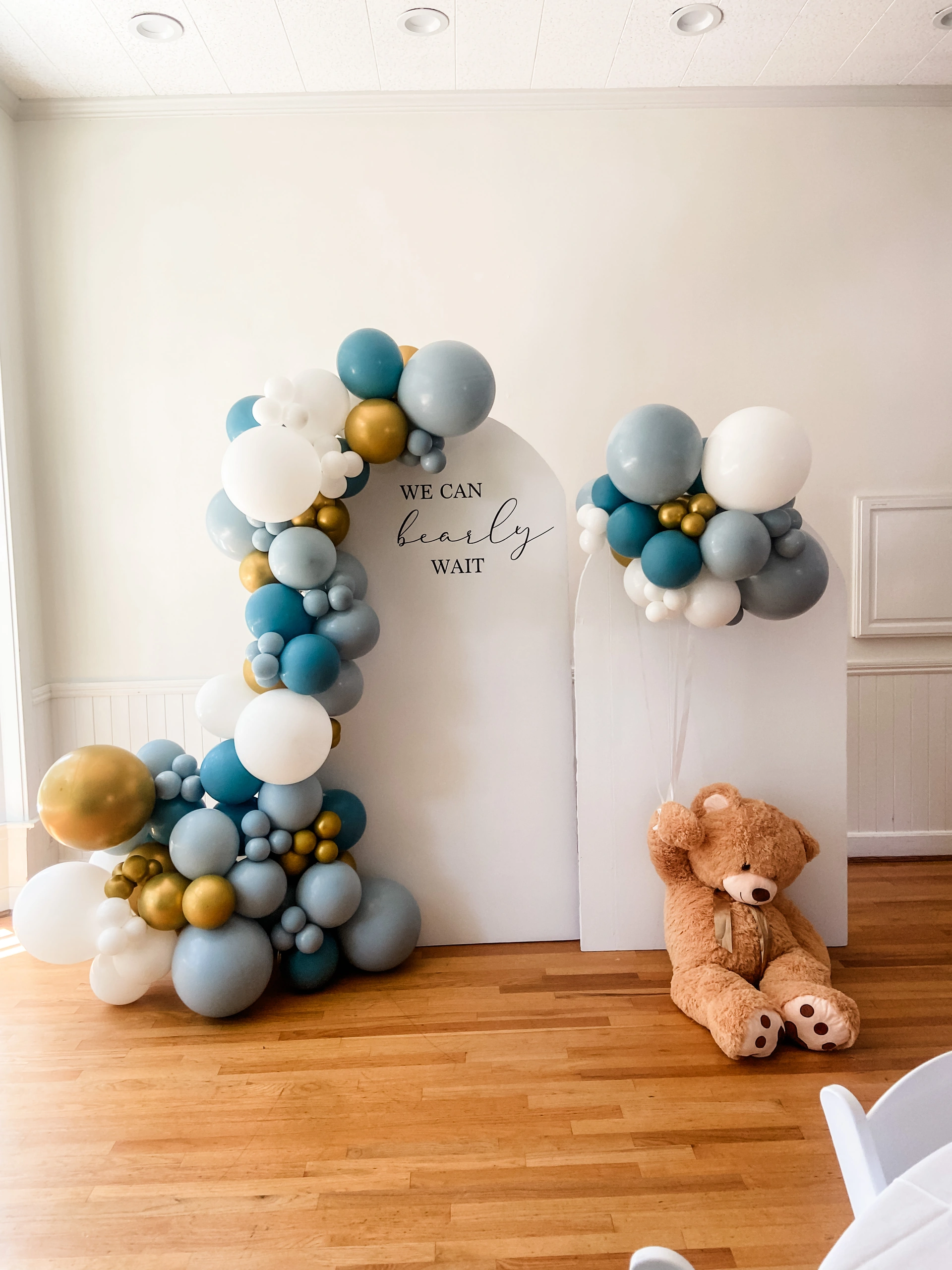 Blue, white and gold balloons with a teddy bear and We Can Bearly Wait backdrop.