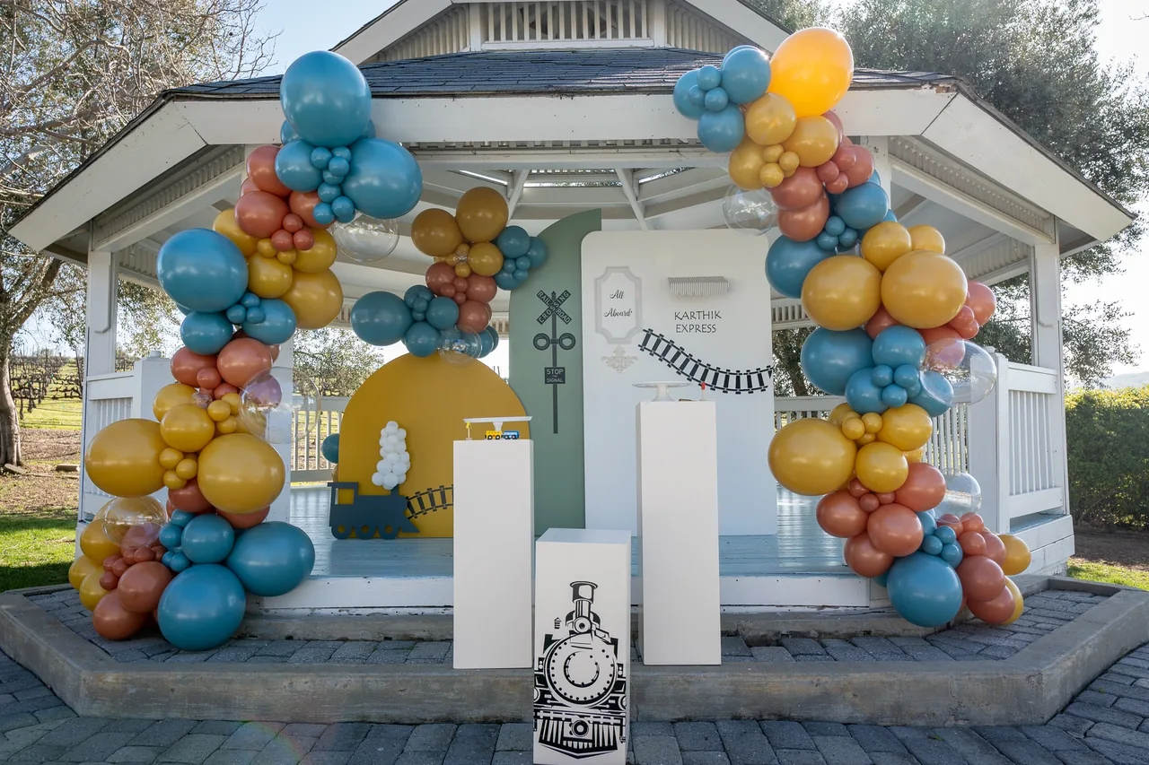 Train-themed birthday balloons and backdrops at a garden gazebo.