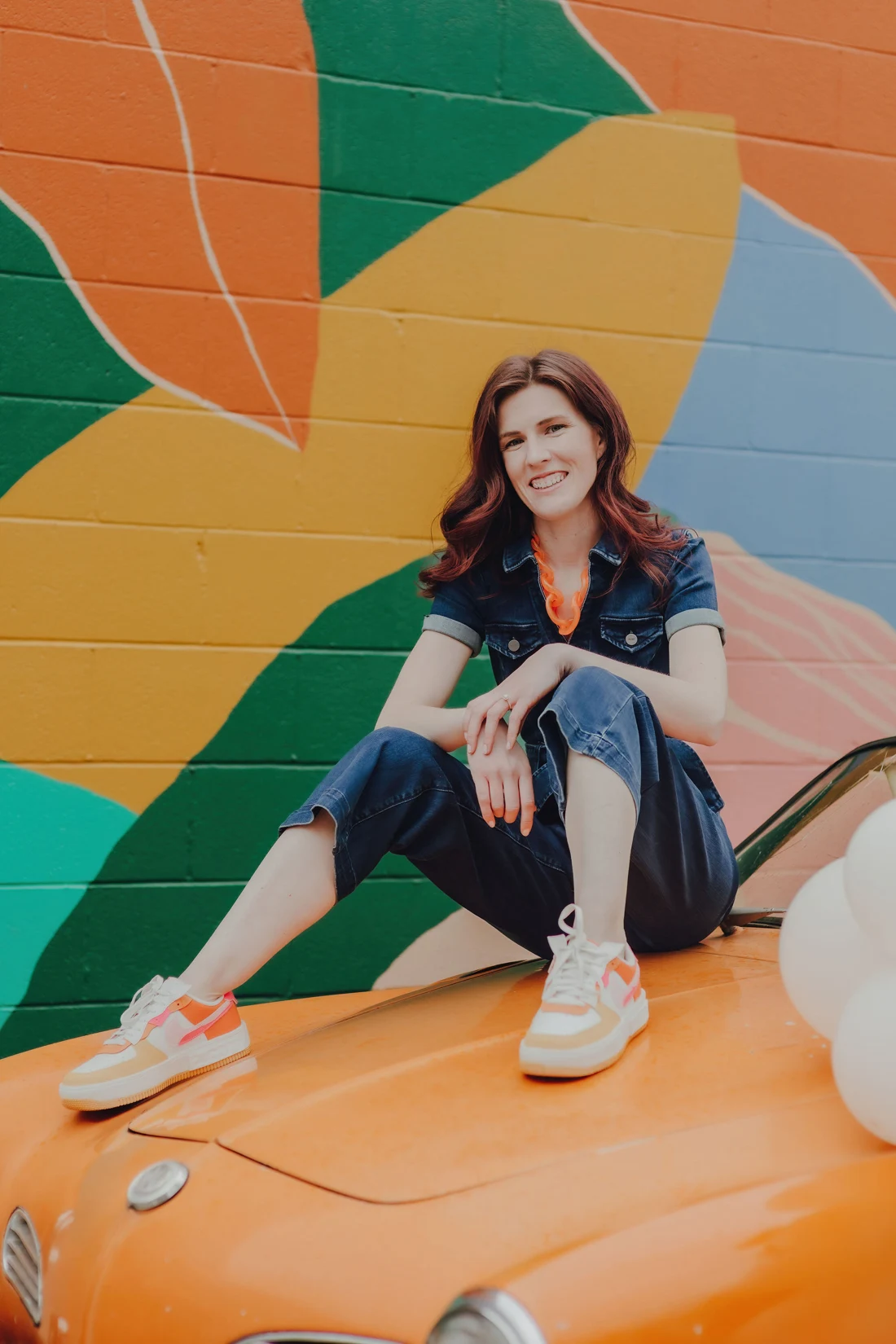 Karlie Vamvouris sitting on an orange vintage convertible in front of a colorful mural.